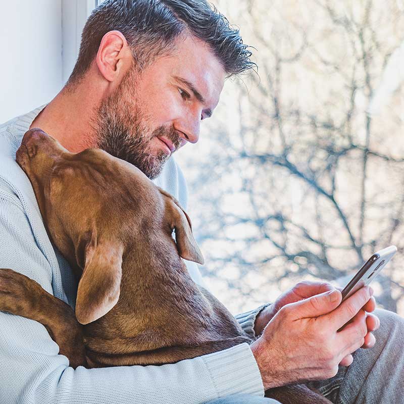 puppy cuddling in man's arms as he makes an appointment via text message